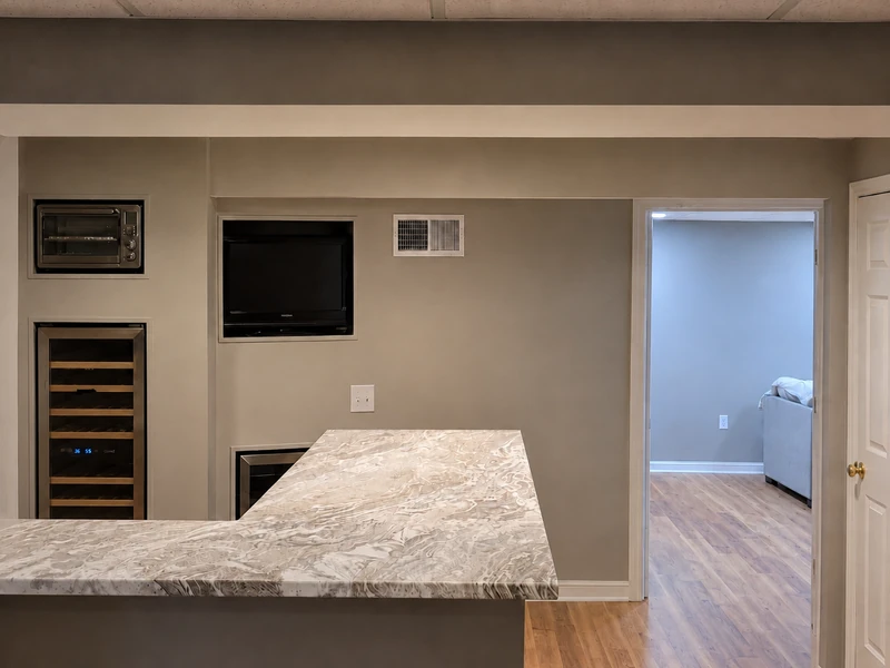Finished basement bar with custom countertop, built-in appliances, and updated flooring by KNA Remodeling